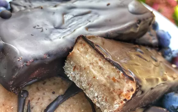 1. Nejdříve si připravíme první vrstvu. Mandle, kokosovou mouku a banán na první vrstvu rozmixujeme. Přimícháme kokosový olej. Vznikne nám těsto, které rozprostřeme do formy (velikost 22x9 cm) s pečicím papírem. Posypeme nasekanými oříšky, které do těsta lehce zatlačíme a dáme do mrazáku.

2. Mezitím si připravíme další vrstvu. Všechny ingredience na druhou vrstvu rozmixujeme, nalijeme na první vrstvu a dáme na 4 hodiny do mrazáku. Poté těsto rozřízneme na tyčinky, rozehřejeme hořkou čokoládu (asi 30-50 g) ve vodní lázni a obalíme tyčinky. Skladujeme v lednici.