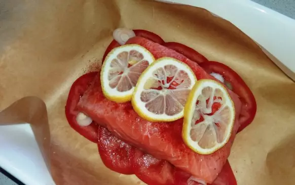 Lososa omyjte a osušte. Na pečicí papír vyskládejte na kolečka nakrájené rajče a posypte kolečky jarní cibulky.
Lososa osolte a opaprikujte z obou stran. Položte na rajčata a pokapte citronovou šťávou. Na povrch položte několik koleček citronu.