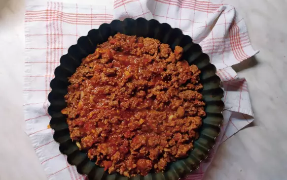 Na pánvi si orestujeme obě mletá masa, osolíme a okořeníme. Přidáme nakrájená pasterizovaná rajčata (lze použít i čerstvá, ale je zapotřebí je spařit a oloupat). Pod pokličkou necháme dusit asi 30 minut. Občas promícháme. Že máme hotovo poznáme podle toho, že se nám zredukuje tekutina a zůstane nám hustá směs. 
Mezitím, co nám směs probublává, nakrájíme si celer a mrkev na kostičky a v osolené vodě vaříme do měkka. Poté scedíme a za postupného přilévání smetany vyšleháme do hustějšího pyré. 
Do koláčové formy dáme nejdříve směs z mletého masa, poté posypeme nastrouhaným sýrem a nakonec pokryjeme celerovo-mrkvový pyré. Pečeme v předem vyhřáté troubě na 180°C 40-45 minut.