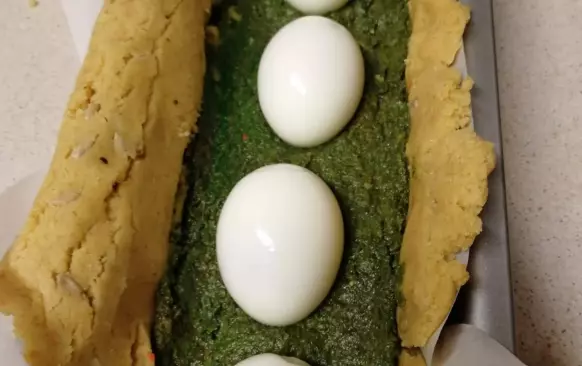 Pozor těsto je křehké, mělo by být alespoň 5 mm tlusté i více. Při vkládání do formy se může trochu potrhat, ale vzhledem k tomu, že tato strana bude spodní, tak to nevadí.

Na těsto navrstvíme polovinu špenátu a naskládáme za sebou vařená vejce a pokryjeme zbytkem špenátu.

Opatrně překryjeme těstem, které nám přesahuje formu.