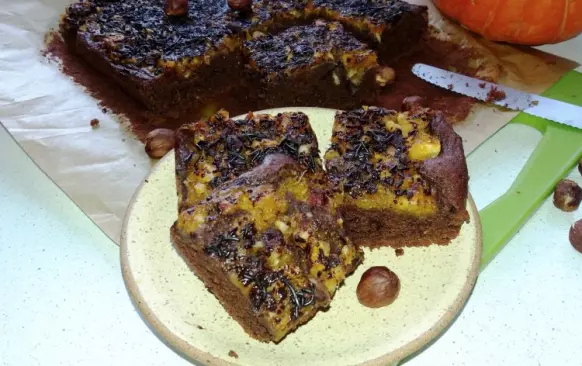Těsto vylijte na plech vyložený pečicím papírem. Dýňové pyré smíchejte s medem, ořechy a špetkou skořice a touto směsí polijte povrch těsta. Celé posypte po povrchu zbytkem nastrouhané čokolády. Pečte v předehřáté troubě na 180 °C cca 40 minut.