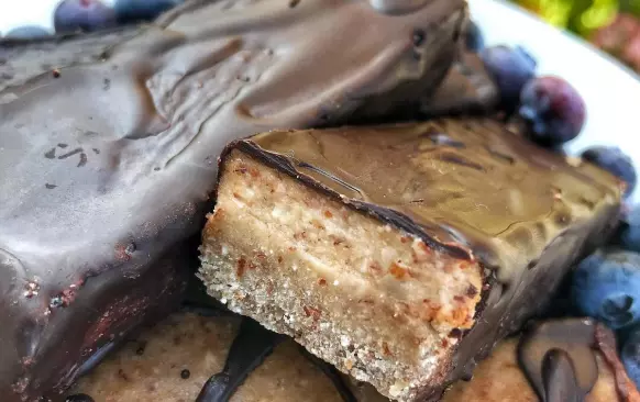 1. Nejdříve si připravíme první vrstvu. Mandle, kokosovou mouku a banán na první vrstvu rozmixujeme. Přimícháme kokosový olej. Vznikne nám těsto, které rozprostřeme do formy (velikost 22x9 cm) s pečicím papírem. Posypeme nasekanými oříšky, které do těsta lehce zatlačíme a dáme do mrazáku.

2. Mezitím si připravíme další vrstvu. Všechny ingredience na druhou vrstvu rozmixujeme, nalijeme na první vrstvu a dáme na 4 hodiny do mrazáku. Poté těsto rozřízneme na tyčinky, rozehřejeme hořkou čokoládu (asi 30-50 g) ve vodní lázni a obalíme tyčinky. Skladujeme v lednici.