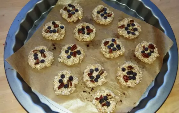 Vytvořte si z hmoty kuličky, které naskládejte na pečicí papír.
Poté je lžičkou či prsty rozmáčkněte do tvaru sušenky a pokud jste čokoládu a ořechy nezapracovali do hmoty, teď je na ně čas. Nezapomeňte je trošku do hmoty vtlačit.